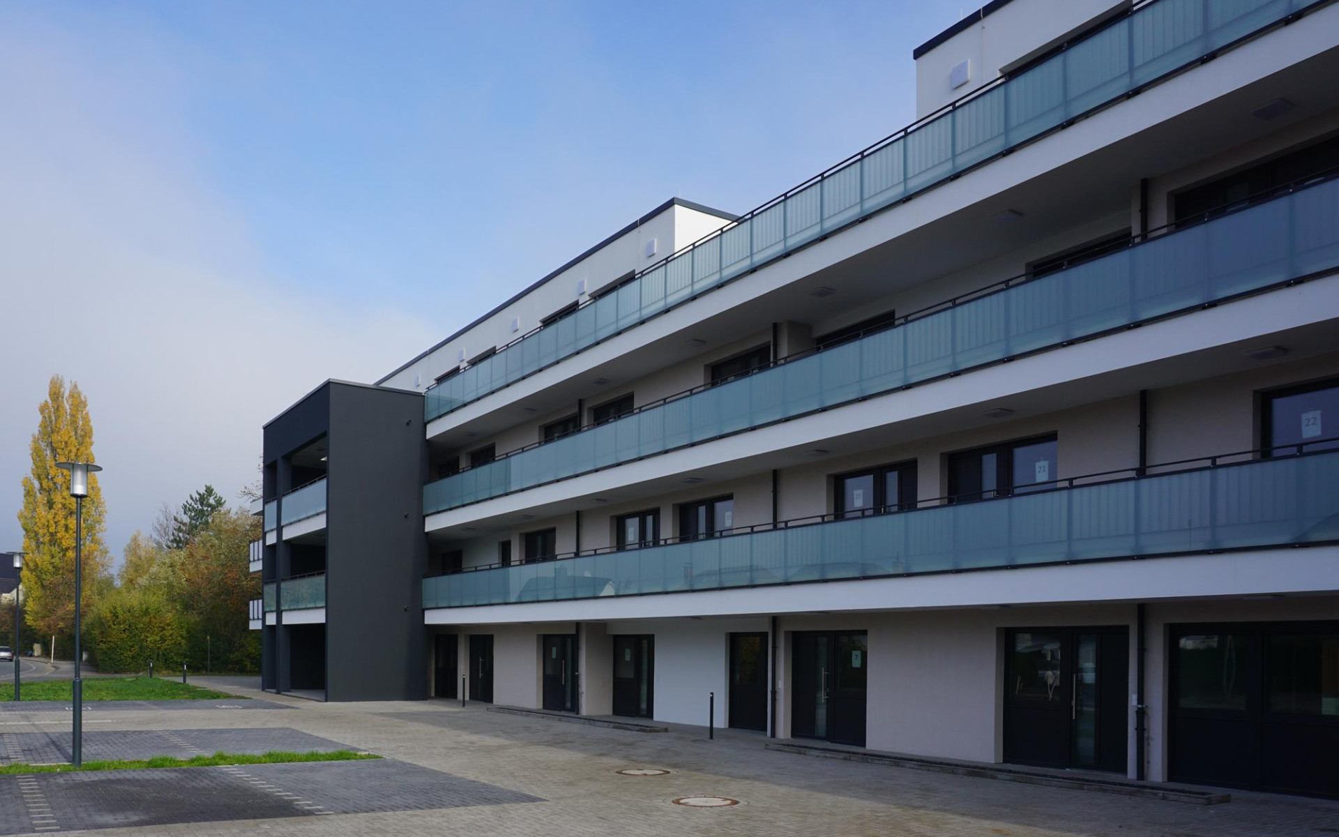 Moderne Wohnanlage mit mehreren Balkonen, umgeben von Grünflächen unter einem bewölkten Himmel.
