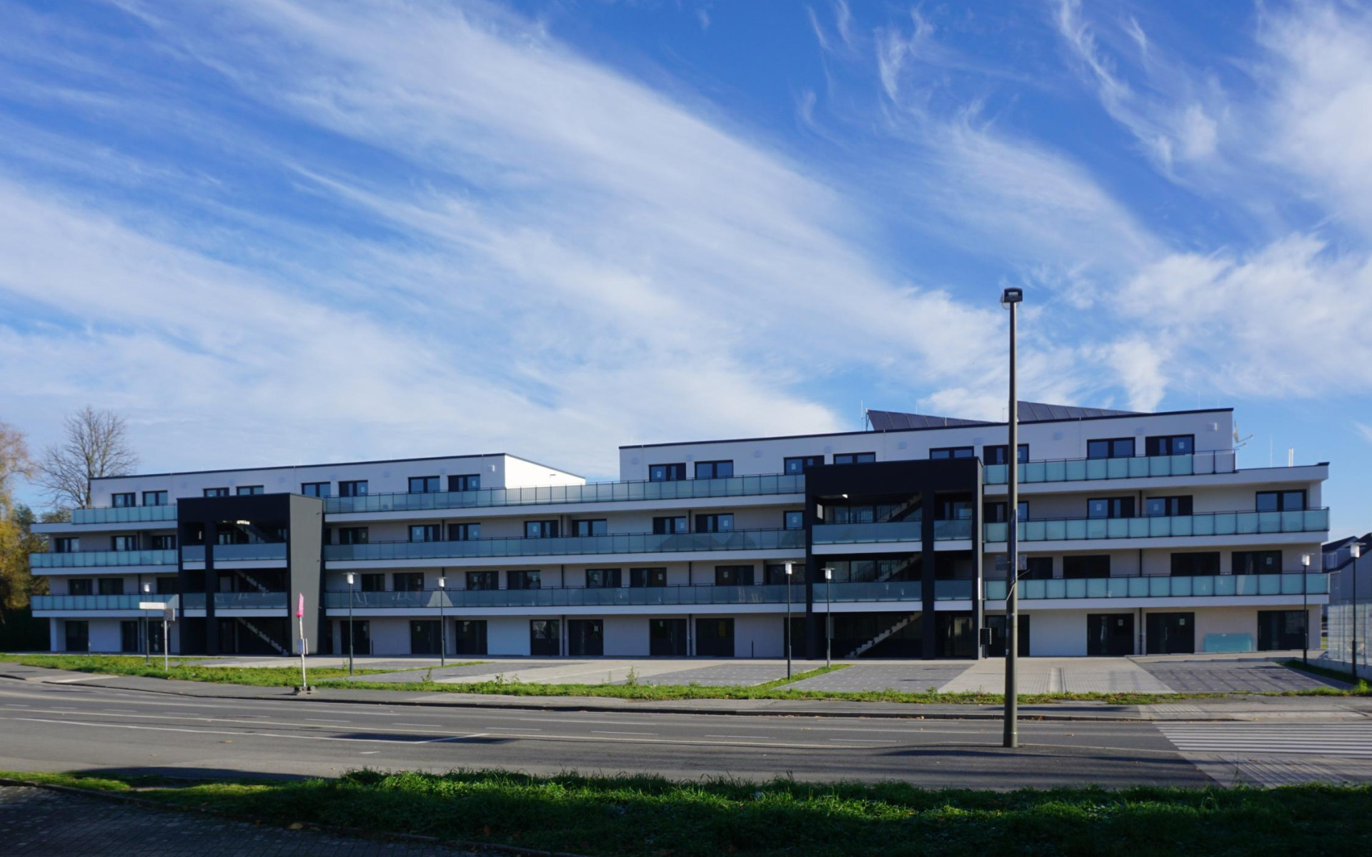 Moderne, mehrgeschossige Wohnanlage mit großen Fenstern und klarer Architektur unter wolkigem Himmel.